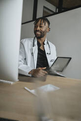 Young doctor with tablet PC practicing telemedicine at desk - MFF08314