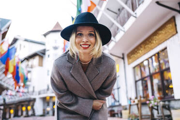 Lächelnde schöne Frau mit Hut und Mantel, die sich in der Stadt bückt - OMIF00168