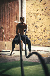 Junger Sportler trainiert mit Battle Ropes im Fitnessstudio zu Hause - ACPF01402
