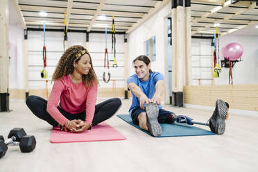 Lächelnde Frau im Gespräch mit einem behinderten Freund beim Training im Fitnessstudio - JCZF00873