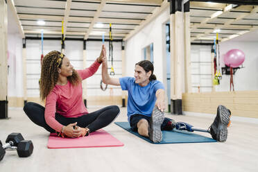 Ein lächelnder behinderter Sportler gibt einem Freund im Fitnessstudio die Hand - JCZF00874