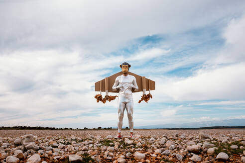 Mann in silbernem Outfit und Affenmaske steht mit Jetpack auf felsigem Boden im Sommer - ADSF31438