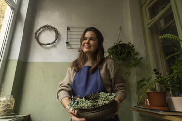 Lächelnde Frau mit Topfpflanze zu Hause - SSGF00224