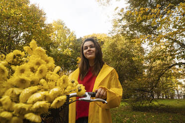 Lächelnde Frau mit gelben Blumen auf dem Fahrrad im Park - SSGF00230