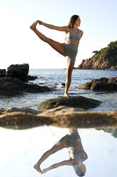 Weibliche Athletin balanciert auf einem Bein am Strand - VEGF05147