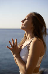 Female athlete with eyes closed meditating at beach - VEGF05150