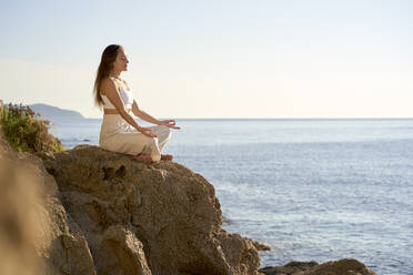 Sportswoman meditating in lotus position on rock at sunset - VEGF05152