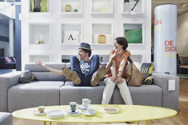 Cheerful couple sitting on sofa in furniture store - RORF02857