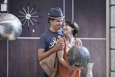 Lächelnder Mann betrachtet seine Freundin, die eine Vase im Laden hält - RORF02863