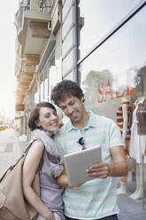 Smiling couple using digital tablet while standing by clothing store - RORF02880