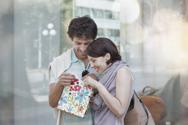 Lächelndes Paar, das beim Einkaufen in die Geschenktüte schaut - RORF02887