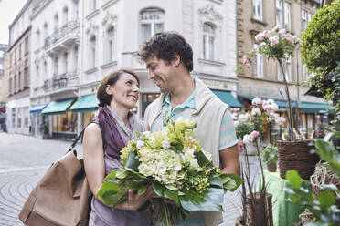 Lächelndes Paar mit Blumenstrauß auf der Straße stehend - RORF02888