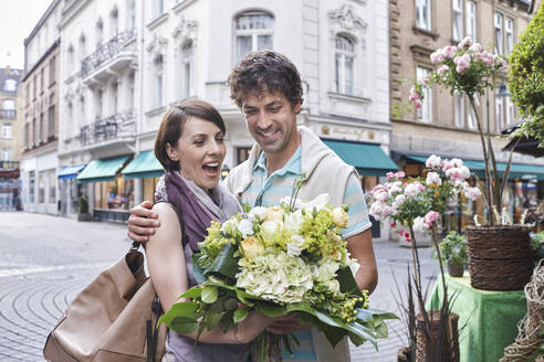 Glückliches Paar mit Blumenstrauß auf der Straße stehend - RORF02889