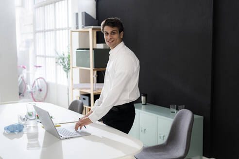 Confident businessman with laptop at desk in office - GIOF14035