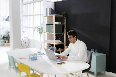 Lächelnder arbeitender Mann mit Laptop am Schreibtisch im Büro - GIOF14037