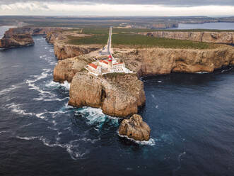 Luftaufnahme des Farol do Cabo de Sao Vicente, eines schönen Leuchtturms auf einer Klippe bei Sonnenuntergang mit Blick auf den Ozean, Sagres, Algarve-Region, Portugal. - AAEF13299