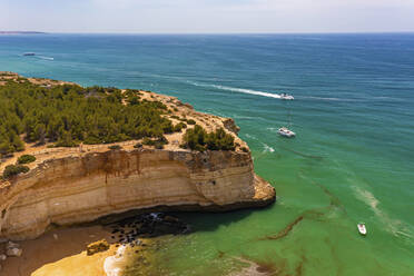 Luftaufnahme eines Bootes, eines Katamarans und einer Yacht, die auf dem Meer in der Nähe der Klippen des Strandes Praia da Corredoura in Lagoa, Algarve, Portugal, kreuzen. - AAEF13310