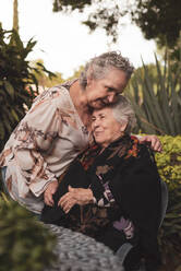 Glückliche ältere Frau umarmt und küsst ihre Schwester auf den Kopf und lächelt dann, während sie gemeinsam Zeit im Garten verbringen - ADSF31488