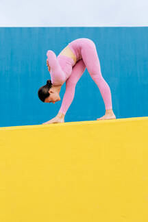 Side view of fit female in pink sportswear practicing yoga in Standing  Forward Bend pose on