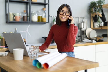 Businesswoman talking on smart phone working at home - GIOF14075