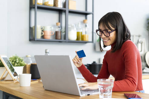 Businesswoman holding credit card working on laptop at home - GIOF14085