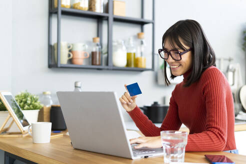 Geschäftsfrau hält Kreditkarte und arbeitet zu Hause am Laptop - GIOF14085