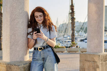 Junge rothaarige Frau schaut auf ihr Handy in einem Seehafen - CAVF95077