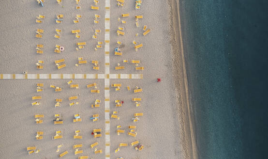 Aerial view of a lido with crossed walkways and closed parasols and sunbeds at sunrise along the coastline in Calabria, Italy. - AAEF13329