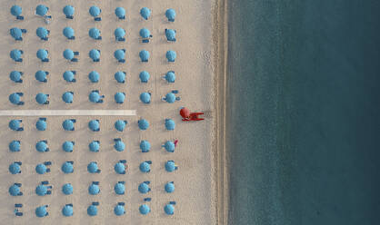 Luftaufnahme eines gut sortierten Strandbads mit blauen Sonnenschirmen und Liegestühlen bei Sonnenaufgang an der Küste in Kalabrien, Italien. - AAEF13330