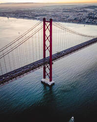 Luftaufnahme der Brücke vom 25. April über den Tejo bei Sonnenuntergang mit der Innenstadt von Lissabon im Hintergrund, Lissabon, Portugal. - AAEF13348