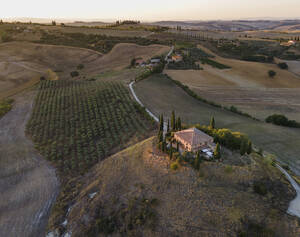 Luftaufnahme eines kleinen Hauses auf einem Hügel, umgeben von einem Weinberg, bei Sonnenuntergang im Val d'Orcia, Toskana, Italien. - AAEF13392