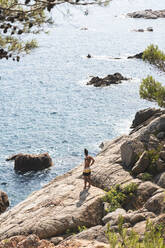 Mann steht auf einem Felsen und schaut aufs Meer, Lloret De Mar, Katalonien, Spanien - JAQF00859