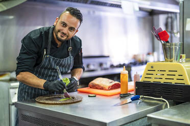 Lächelnder Koch dekoriert Teller für die Präsentation in der Küche eines Restaurants - DLTSF02361