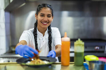 Lächelnde Küchenpraktikantin beim Foodstyling im Restaurant - DLTSF02383