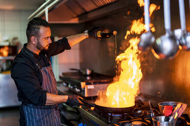 Chef preparing flambe dish on stove in restaurant kitchen - DLTSF02384
