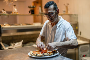 Chefkoch beim Belegen der Pizza in der Küche - DLTSF02389