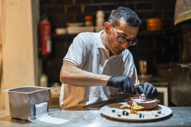 Konzentrierte Köchin beim Dekorieren des Desserts in der Küche - DLTSF02390