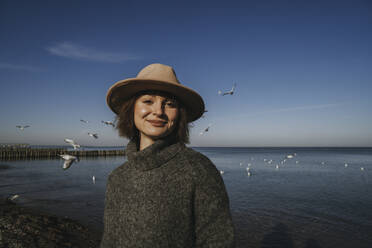 Frau im Rollkragenpulli steht am Meer vor blauem Himmel - SSGF00251