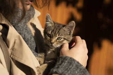 Junge Frau im Mantel streichelt Katze an einem sonnigen Tag - SSGF00252