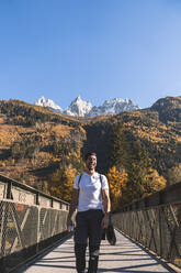 Hiker walking on footbridge in front of French Alps on sunny day, Chamonix, France - JAQF00875