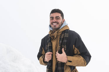 Smiling man hiking wearing warm clothes on snow - JAQF00884