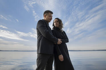 Couple standing together near lakeshore - LLUF00304