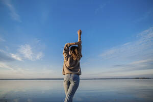Frau mit erhobener Hand schaut auf einen See an einem sonnigen Tag - LLUF00312