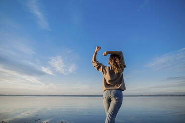 Woman with arms raised standing at lake - LLUF00313