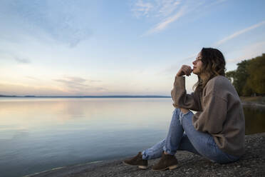 Nachdenkliche Frau sitzt auf einem Felsen und schaut auf den See - LLUF00314