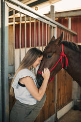 Schwangere Frau kümmert sich um ein Pferd im Stall - GRCF01067