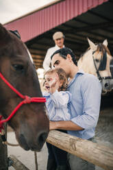 Vater und Tochter sehen sich ein Pferd im Stall an - GRCF01081
