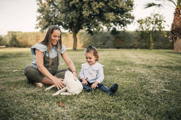 Smiling mother and daughter playing with dog at ranch - GRCF01088