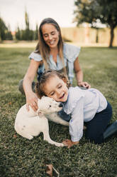 Happy daughter playing with dog while mother in background at ranch - GRCF01090