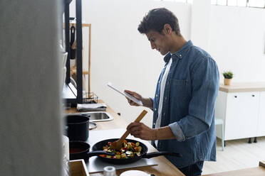 Man using digital tablet while preparing food in kitchen - GIOF14099